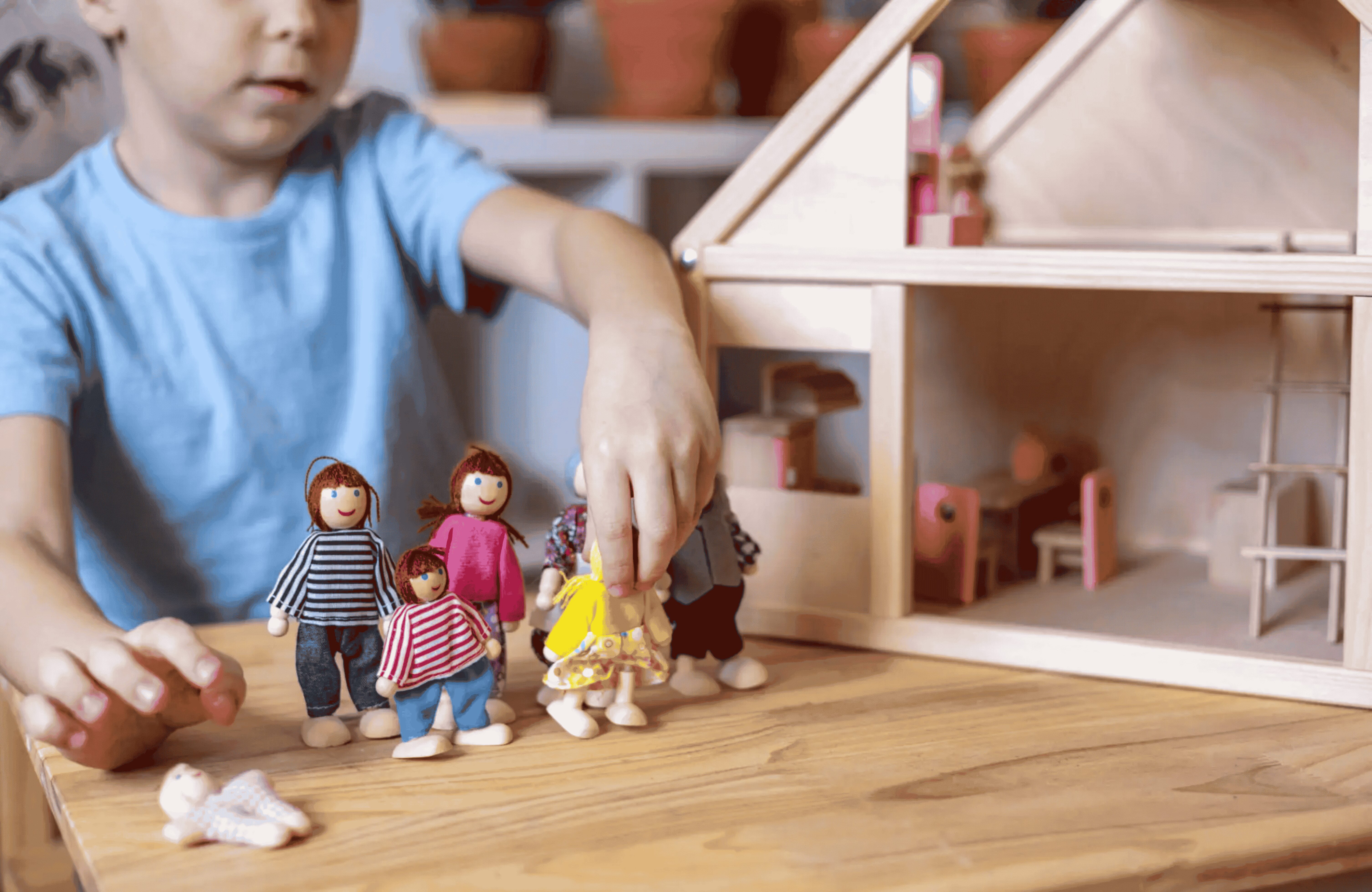67e43ab1b39bf_boy playing with house (1) (1) (1) A child playing with wooden dolls in front of a doll house.