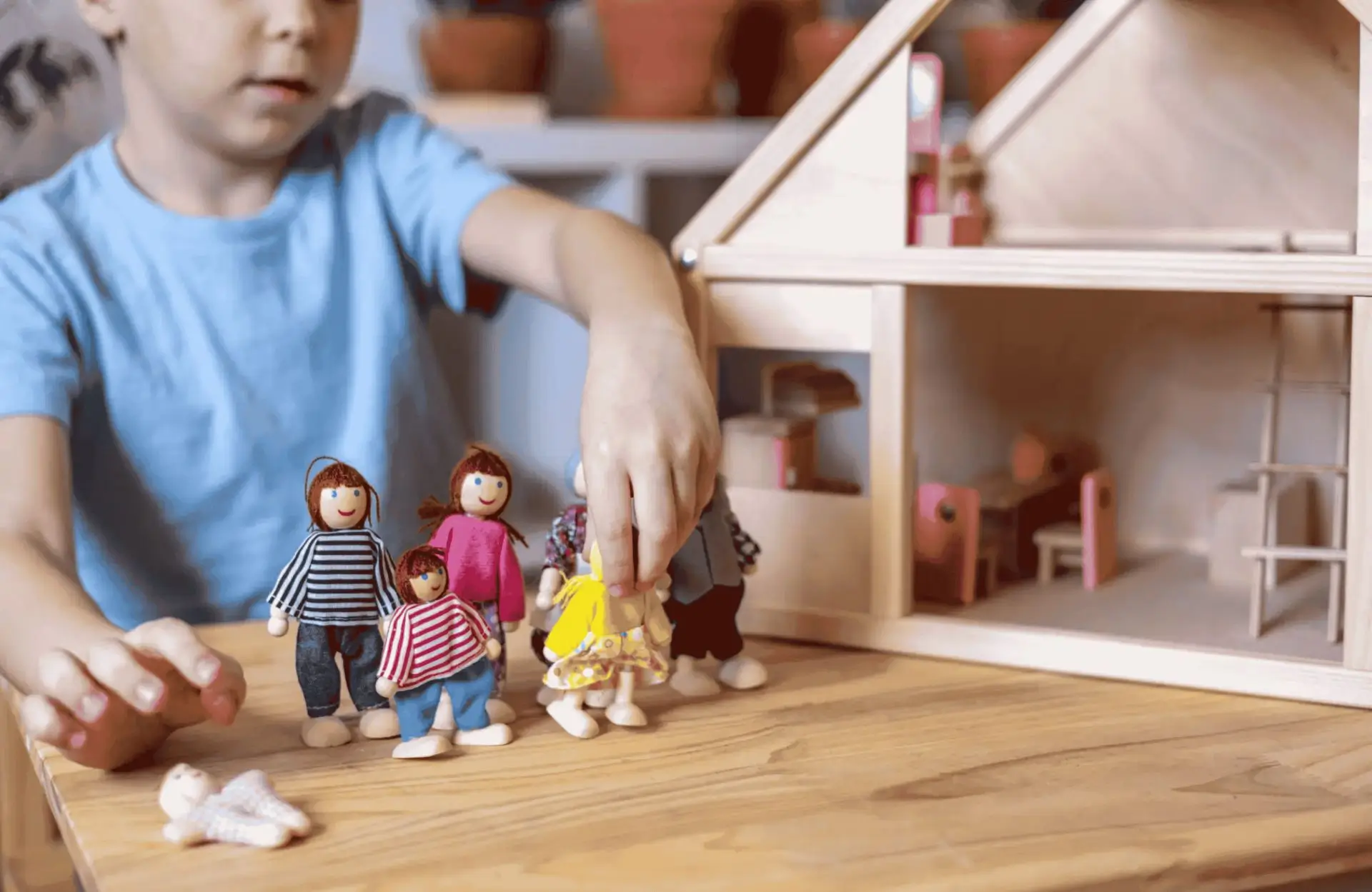 A child playing with wooden dolls in front of a doll house.